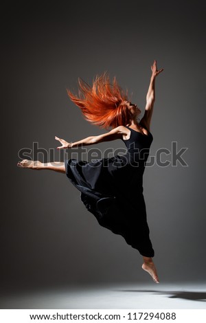 young beautiful dancer with red hair jumping on a dark studio background