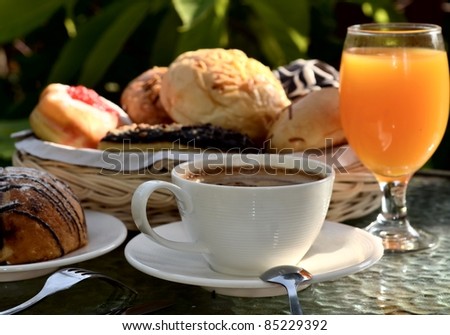 Breakfast table arrangement with  bread, cappuccino and orange juice served as the menu. Illuminated with a warm morning light.