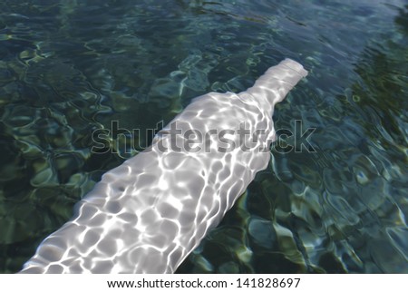 A horizontal photographic image of a white wine bottle under water