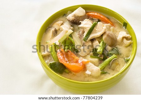 Tom Kha Gai, a traditional dish from Thailand served in a bright green ceramic bowl and set against a white background