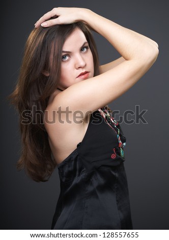 Beautiful young girl in a black blouse. Stand with raised hands to the head. On a gray background