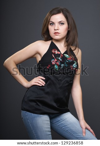 Attractive young woman in a black blouse and blue jeans. On a gray background