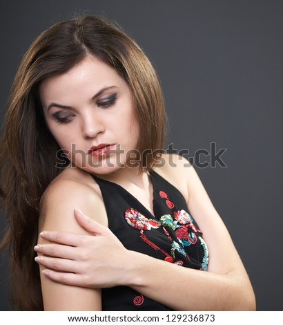 Portrait of attractive young woman in a black blouse. A woman hugs her shoulder and looks down. On a gray background