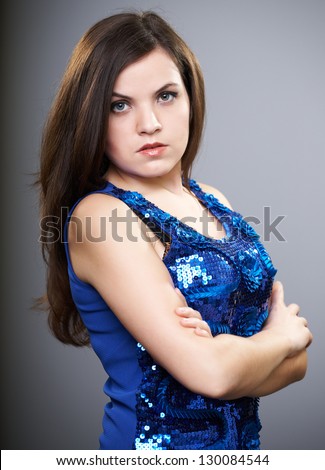 Attractive young woman in a blue shiny dress. Woman standing with folded hands. On a gray background