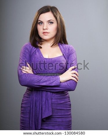 Attractive young woman in a lilac dress. Standing with folded hands. On a gray background