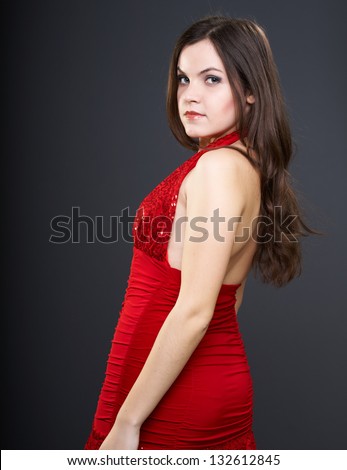 Attractive young woman in a red dress. Woman turned around. On a gray background