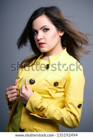 Attractive young woman in a yellow jacket. Hair in motion. On a gray background