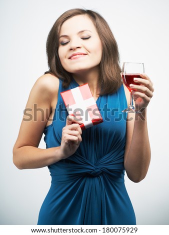 Happy young woman in a blue dress. Holding red gift box and glass of wine. On a gray background