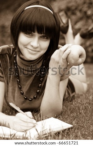 Young beautiful woman lays on field with apple and book
