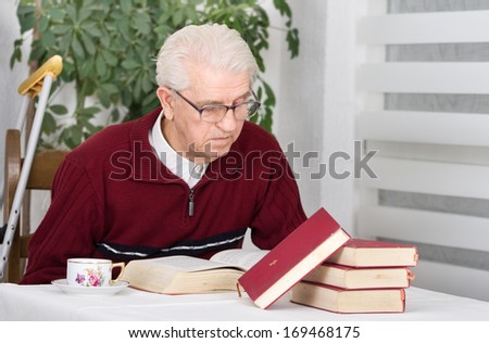 Older man with walking stick sitting in his home and reading books