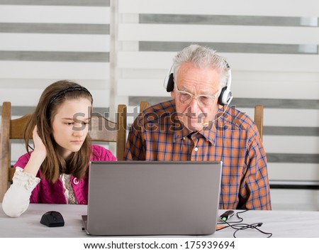 Granddaughter helping grandpa to make on line communication on laptop