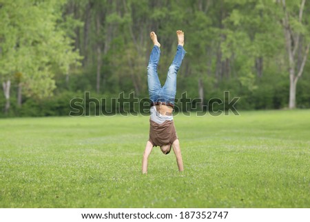 Happy young man standing upside down on grass in forest