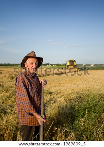 Smiling old peasant standing on field with combine in background
