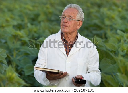 Old agronomist in white coat looking ahead in field