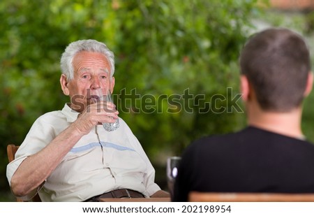 Old man drinking water in garden while sitting with grandson