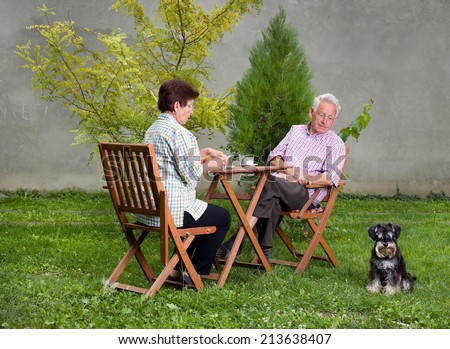 Senior couple with dog sitting in garden at table and having coffee and snack