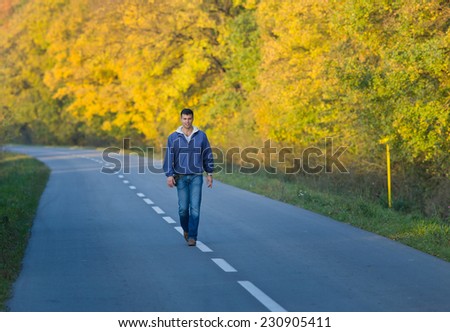 Young attractive man walking on road in forest in fall time