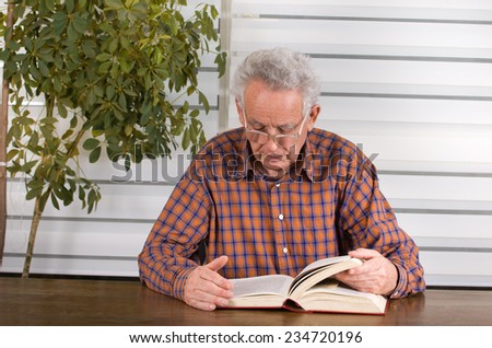 Old man with reading glasses reading book in his library