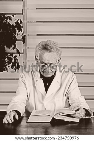 Old photo of senior man in white coat reading book in office
