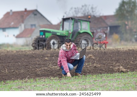Young farmer with laptop on the field with seedlings in late autumn