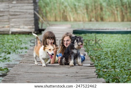 Two girls with dogs lying on wooden dock on the lake