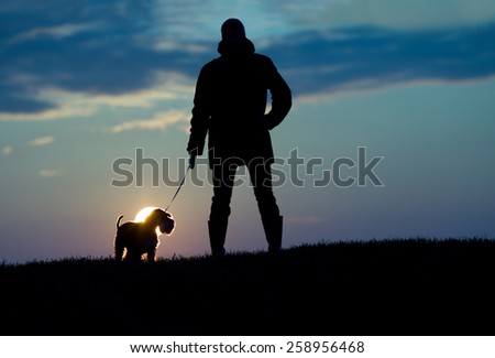 Silhouette of young man in jacket walking dog in the evening