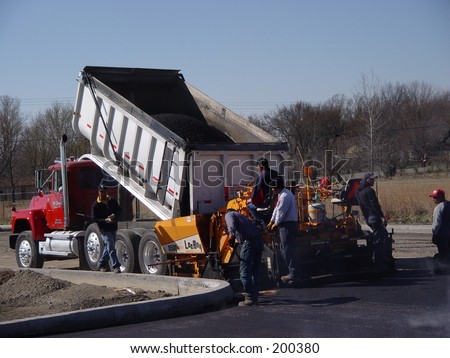 Asphalt spreader being filled by a dump truck.