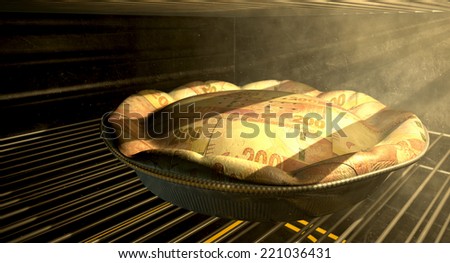 A closeup concept of a money pie made with South African Rand bank notes baking in a heated oven