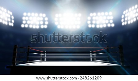 An boxing ring surrounded by ropes spotlit by floodlights in an arena setting at night
