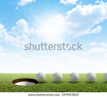 A perfectly manicured golf putting green showing a ball in motion on its way to the hole in the daytime on a blue sky background