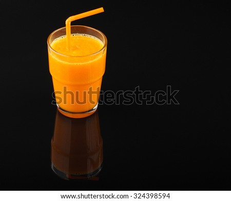 pumpkin smoothie in glass with drinking straw  on black acrylic sheet with reflection on black background