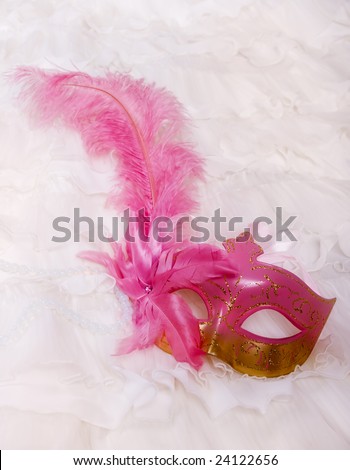 A masquerade mask with a pink ostrich feather and pearl beads on a lacy white ball dress