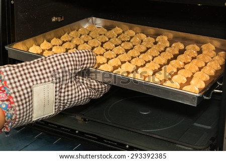 woman\'s hand putting a tray of raw pastry in the oven