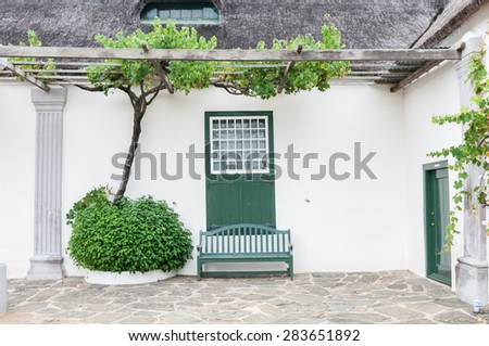 SWELLENDAM, SOUTH AFRICA - DECEMBER 26, 2014: Grape vine, bench and window with barn doors at the historic  Drosdy, built by the Dutch East India Company in 1747