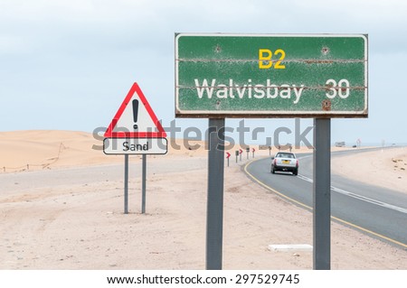 SWAKOPMUND, NAMIBIA - JUNE 22, 2012: A rusted distance marker and a warning against sand on the road between Swakopmund and Walvisbay in Namibia