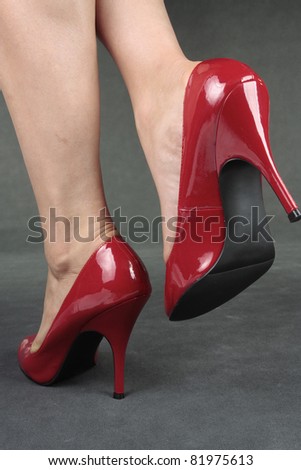 Beautiful female legs wearing red heels over grey background