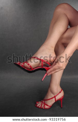Woman legs putiing on red heels   over grey background