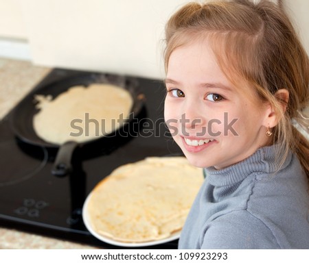 Child bakes pancakes in the kitchen. Girl cooking breakfast