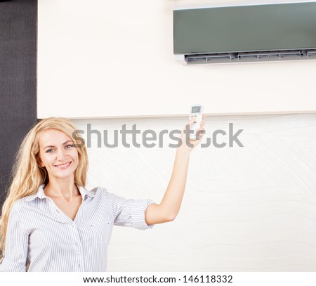 Female holding a remote control air conditioner at home. Happy young woman on sofa