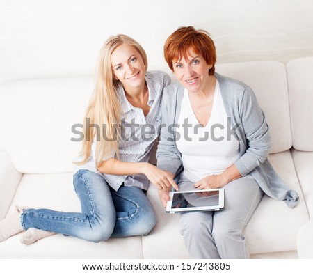 Mother and daughter wiht tablet at sofa. Two women with tablet computer. Family at home on sofa