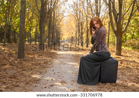 young woman sitting on a suitcase and talking on the phone
