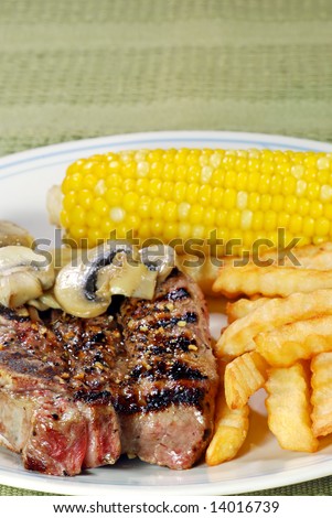 barbecue short ribs with fries and vegetables on a green tablecloth