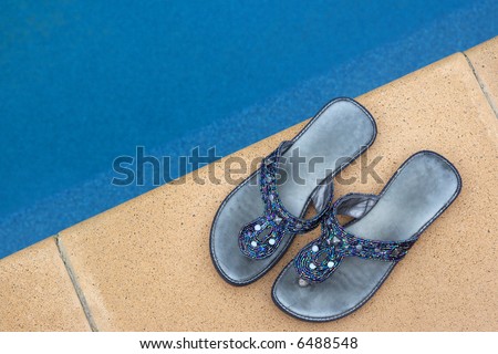 A pair of fashionable ladies slip-on shoes, next to the pool.