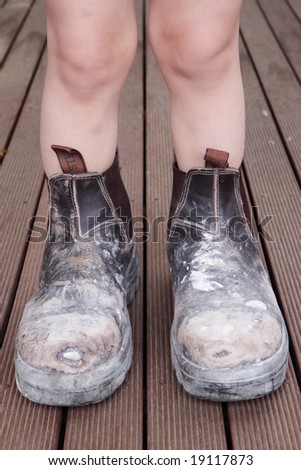 A young boy standing in dad\'s work boots.