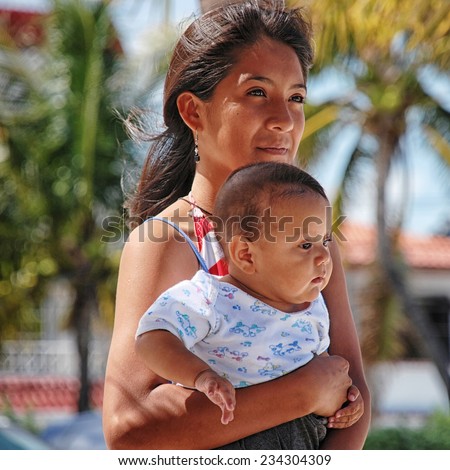 CANCUN, MEXICO - MARCH 27, 2011: Beautiful mexican woman with a child at a famous beach of Yucatan Peninsula. Both facing away from camera, palm trees at the background