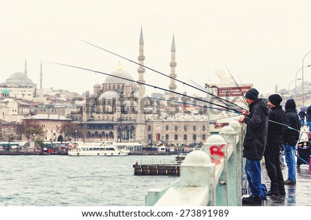 ISTANBUL, TURKEY - DECEMBER 12, 2014: Fishermen at the famous Galata bridge in the cold rainy day with Mosque at the background