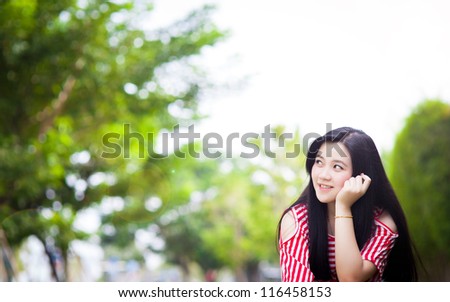 Portrait of dark-haired pensive beautiful young woman in red blouse close up, against green of summer park.
