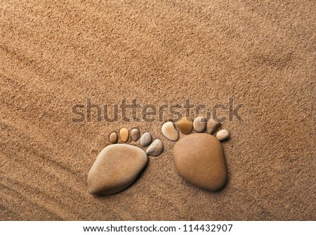 two trace feet made of a pebble stone on the sea sand desert , texture backdrop
