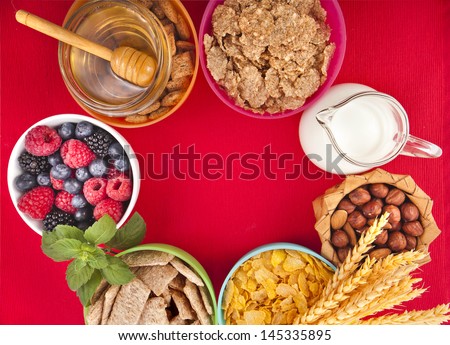 Border top view of  bowl with corn flakes, fresh berries, honey, diet weight loss breakfast concept,  on red background