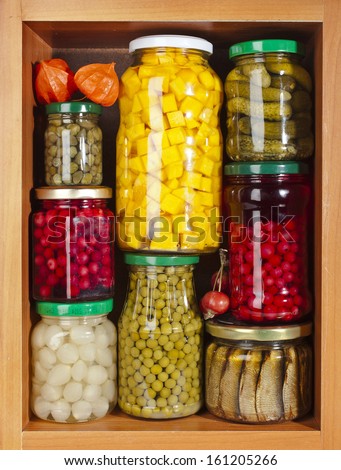 many set glass bottles with preserved food in wooden cabinet